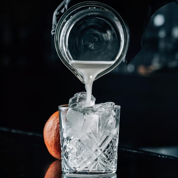 A bartender pours a light-colored cocktail from a mixing glass into an ice-filled glass.