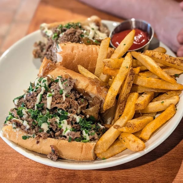 Two cheesesteak sandwiches with fries and ketchup on a white plate at The Social on Morton.