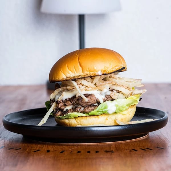 The Social on Morton's burger with two patties, lettuce, crispy onions, and white sauce on a black plate.