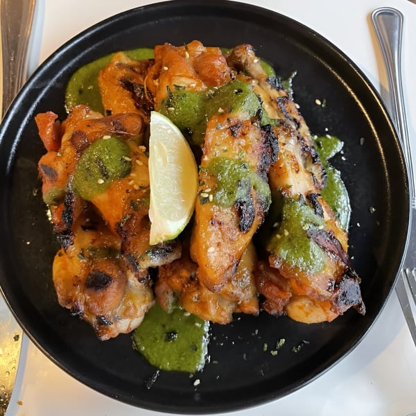 Grilled chicken pieces with green sauce and a lime wedge on a black plate.