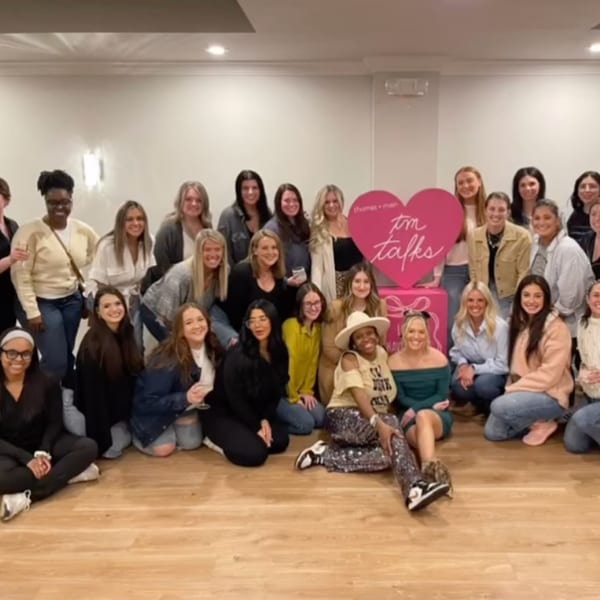 A large group of women posing for a photo in front of a pink heart-shaped sign.