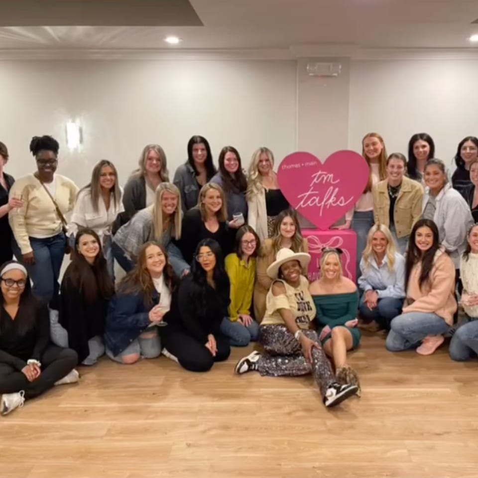 A large group of women posing for a photo in front of a pink heart-shaped sign.